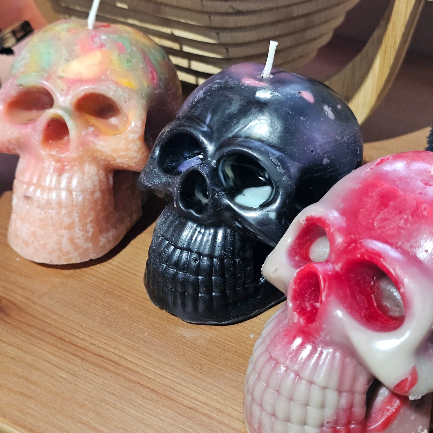 Skull-shaped candles in various colors on a wooden surface