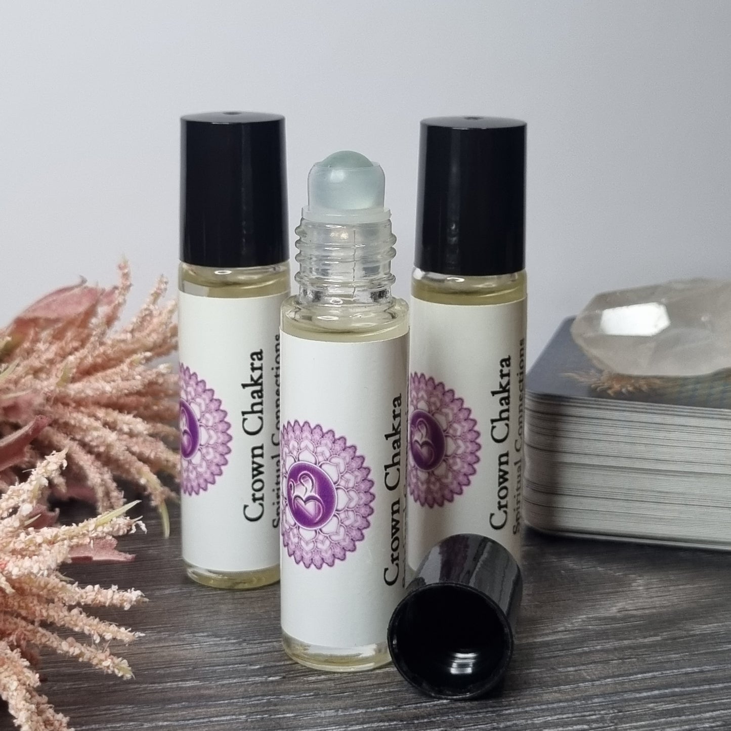 Three rollerball bottles with a purple flower design on a wooden surface.