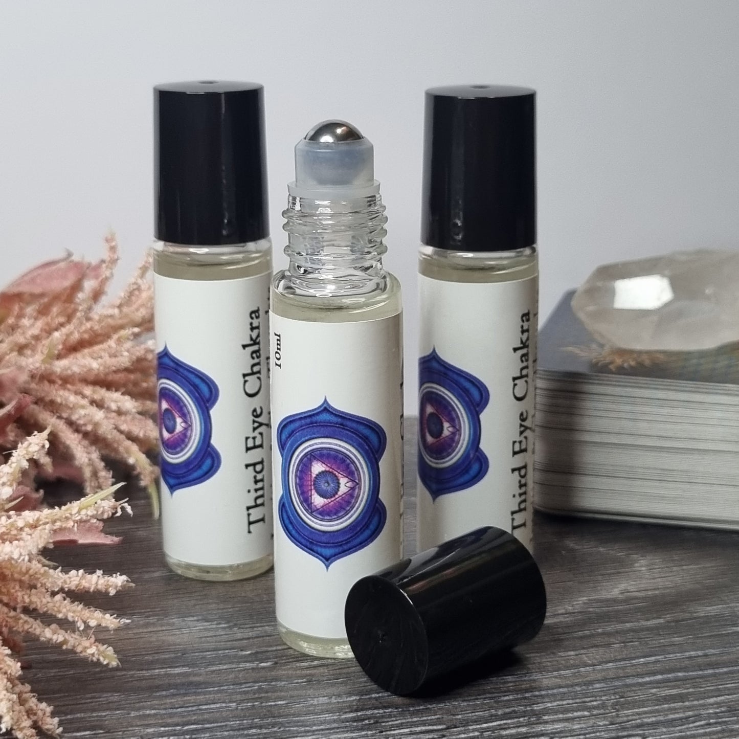 Three rollerball bottles with a third eye chakra design on a wooden surface.