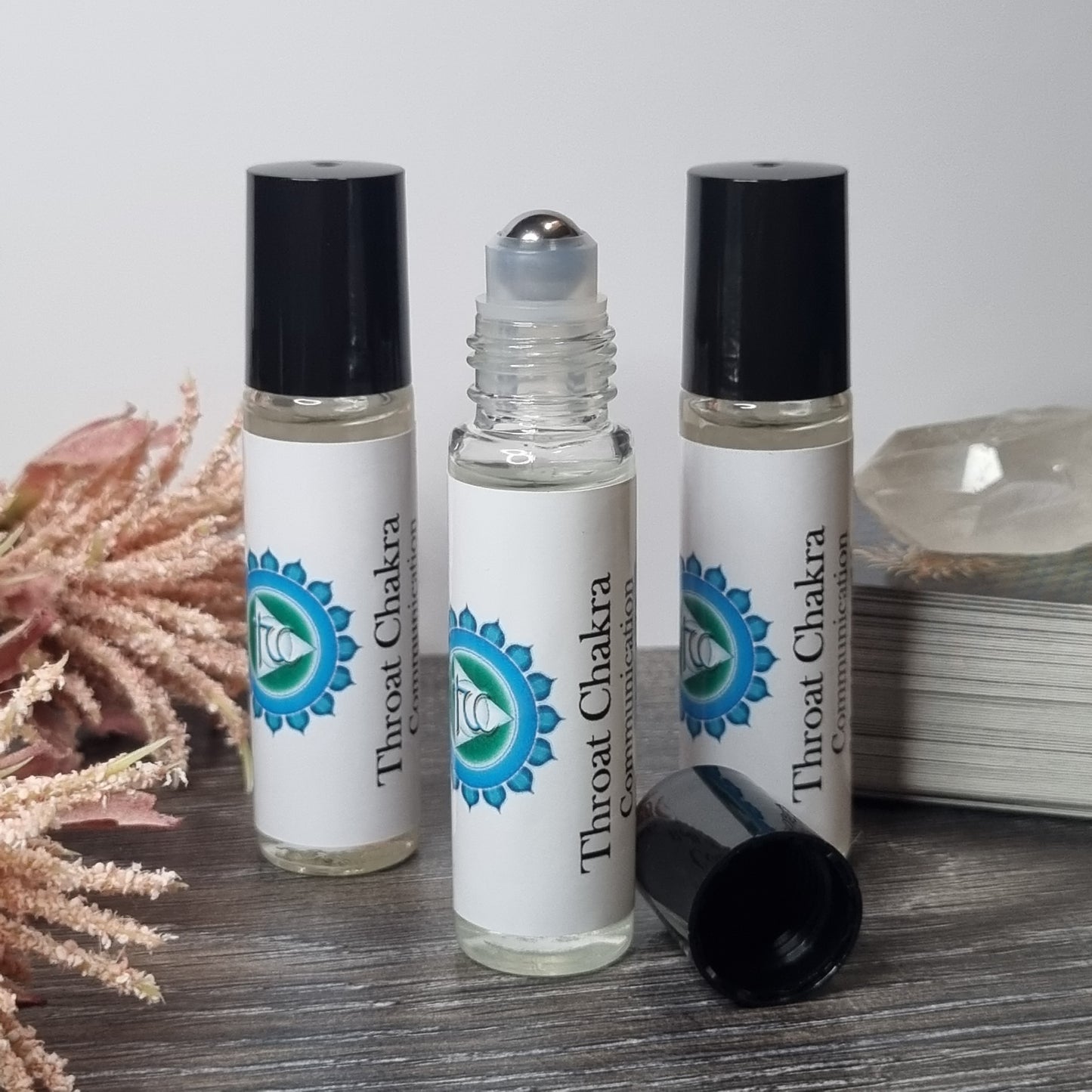Three Throat Chakra rollerball bottles on a wooden surface with a white background